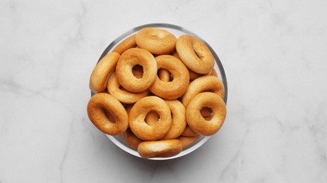 Photo of Bowl of tasty dry bagels (sushki) on white marble table, top view