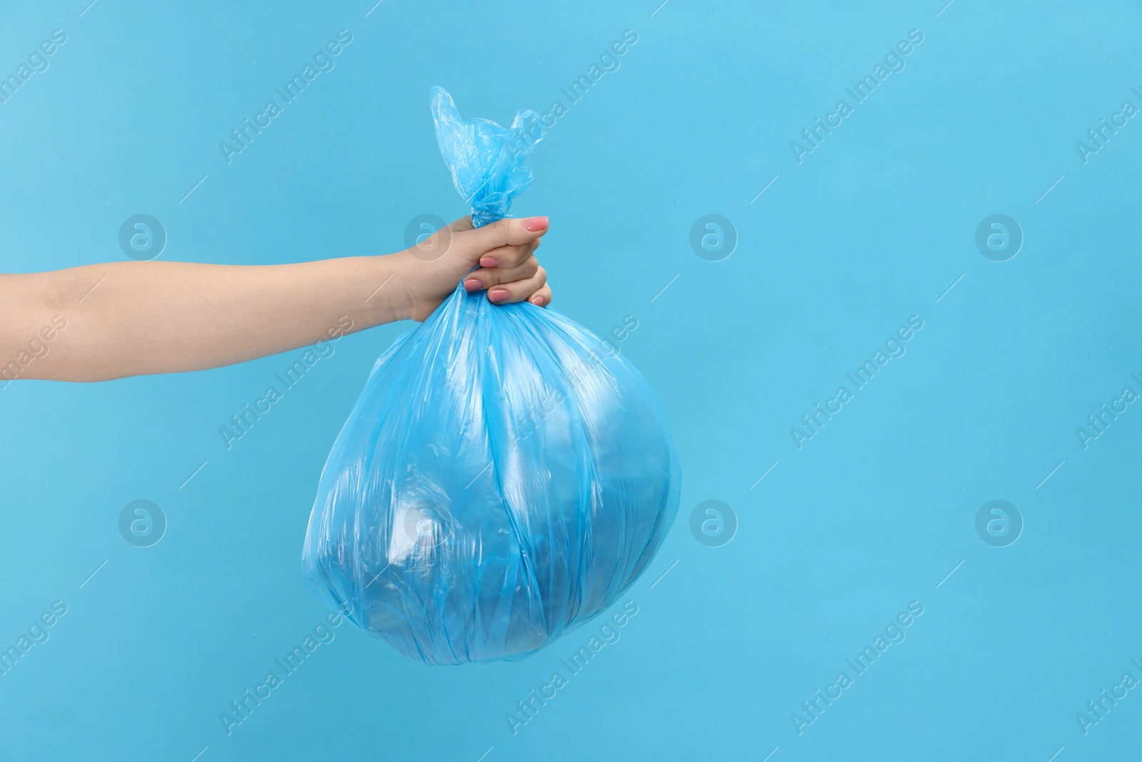 Photo of Woman holding plastic bag full of garbage on light blue background, closeup. Space for text