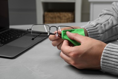 Photo of Man wiping glasses with microfiber cloth at light grey table, closeup