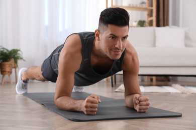 Photo of Handsome man doing plank exercise on yoga mat at home