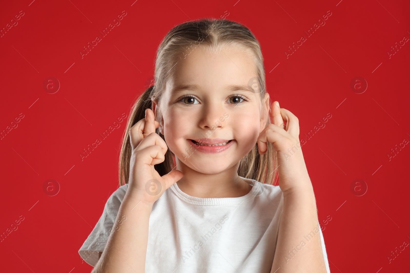 Photo of Child with crossed fingers on red background. Superstition concept