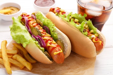 Delicious hot dogs with lettuce, onion and pickle served on white wooden table, closeup