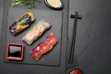 Photo of Delicious rolls wrapped in rice paper served on black table, flat lay. Space for text