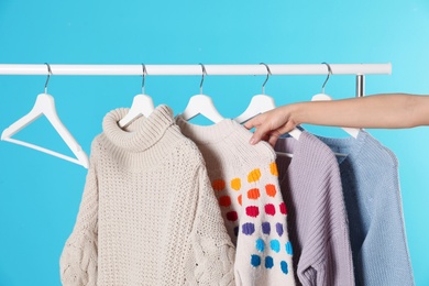 Photo of Woman choosing sweater on rack against color background