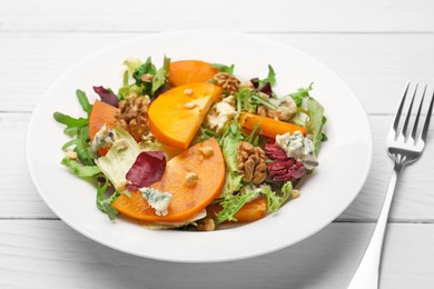 Photo of Delicious persimmon salad and fork on white wooden table, closeup