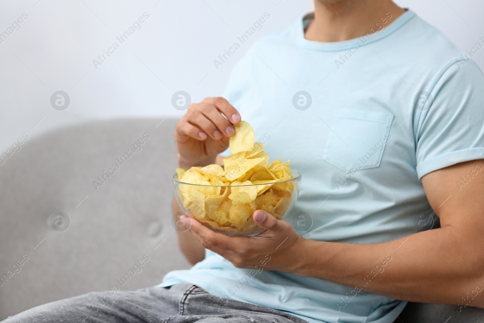 Photo of Man with bowl of potato chips on grey sofa, closeup