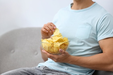 Photo of Man with bowl of potato chips on grey sofa, closeup