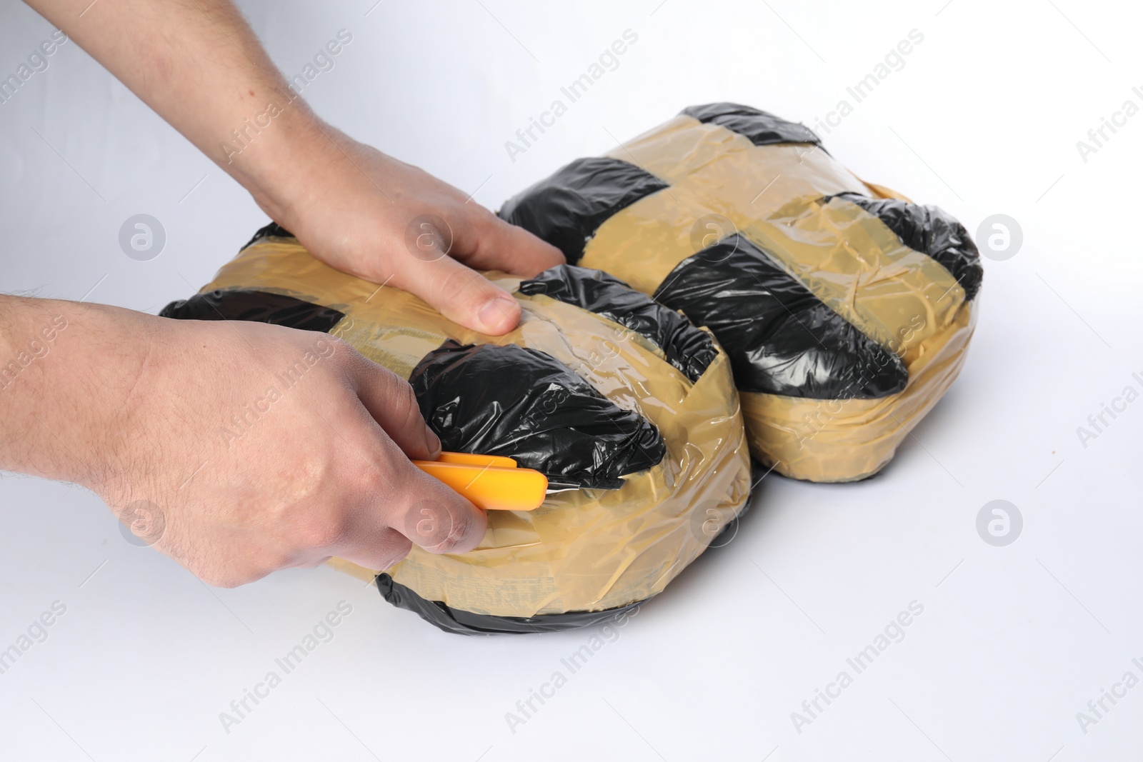 Photo of Smuggling and drug trafficking. Man opening package of narcotics with box cutter on white background, closeup