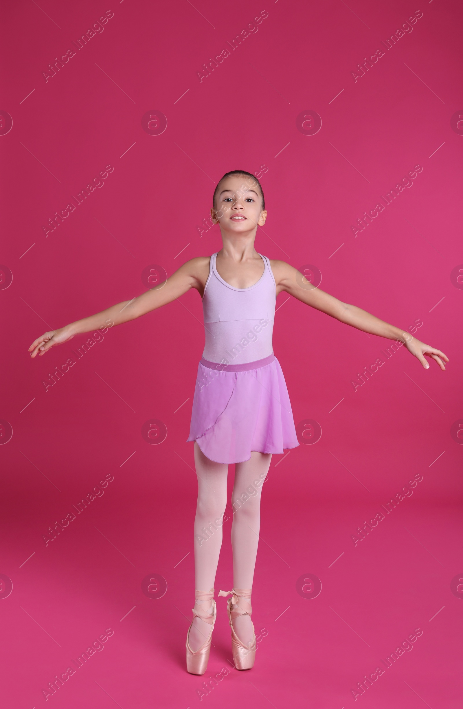 Photo of Little ballerina practicing dance moves on pink background