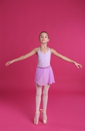 Photo of Little ballerina practicing dance moves on pink background