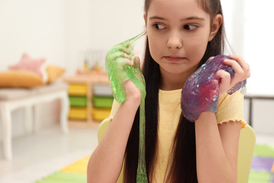 Photo of Emotional little girl playing with slime in room