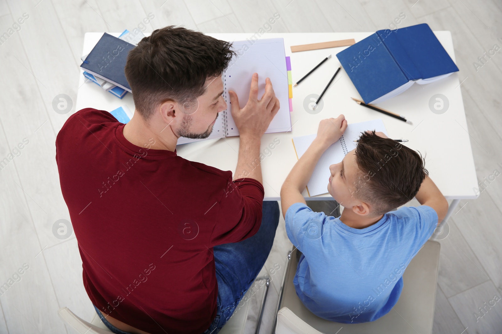 Photo of Dad helping his son with homework in room, above view