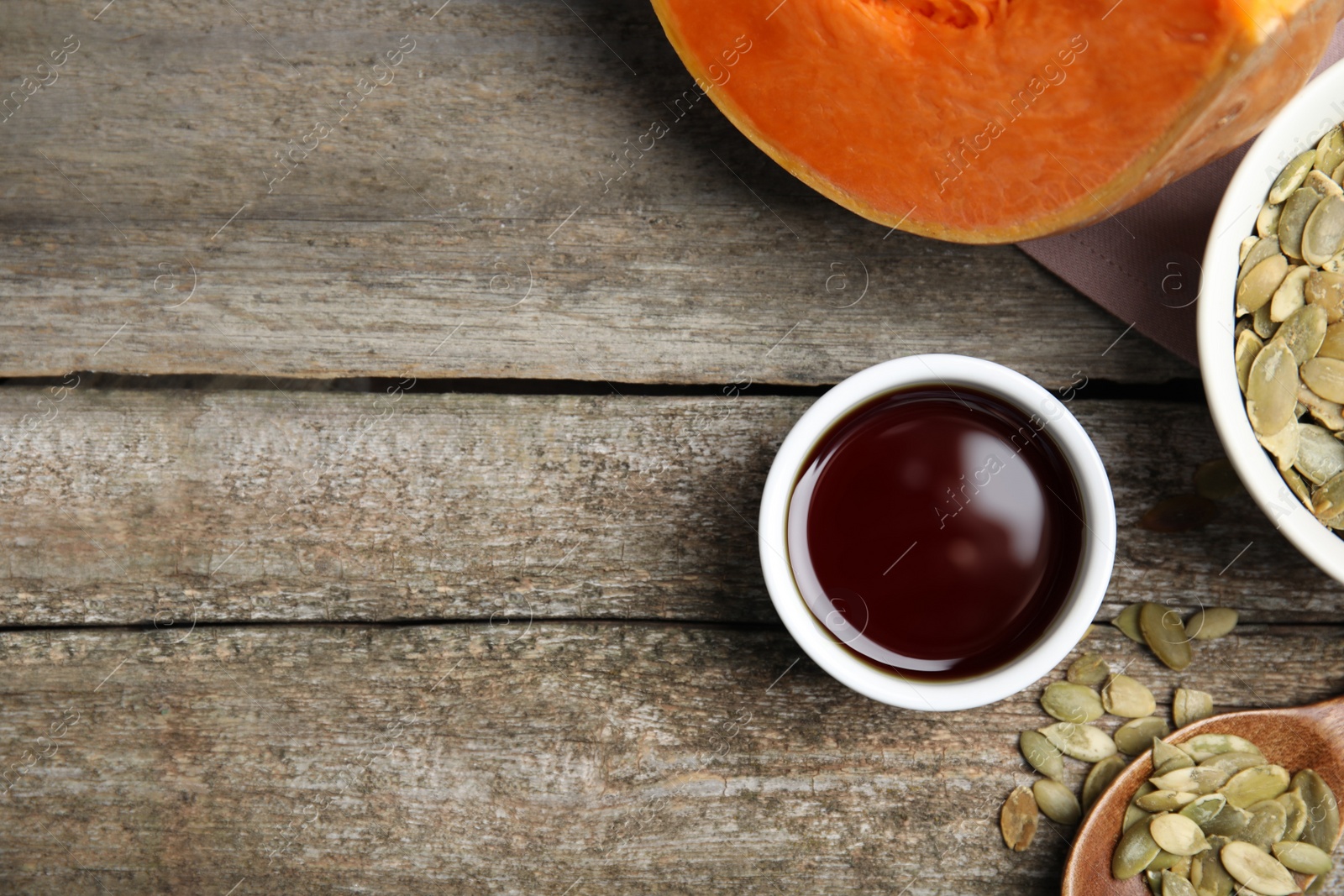 Photo of Bowl of oil and pumpkin seeds on wooden table, flat lay. Space for text