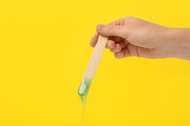 Photo of Woman holding spatula with hot depilatory wax on yellow background, closeup