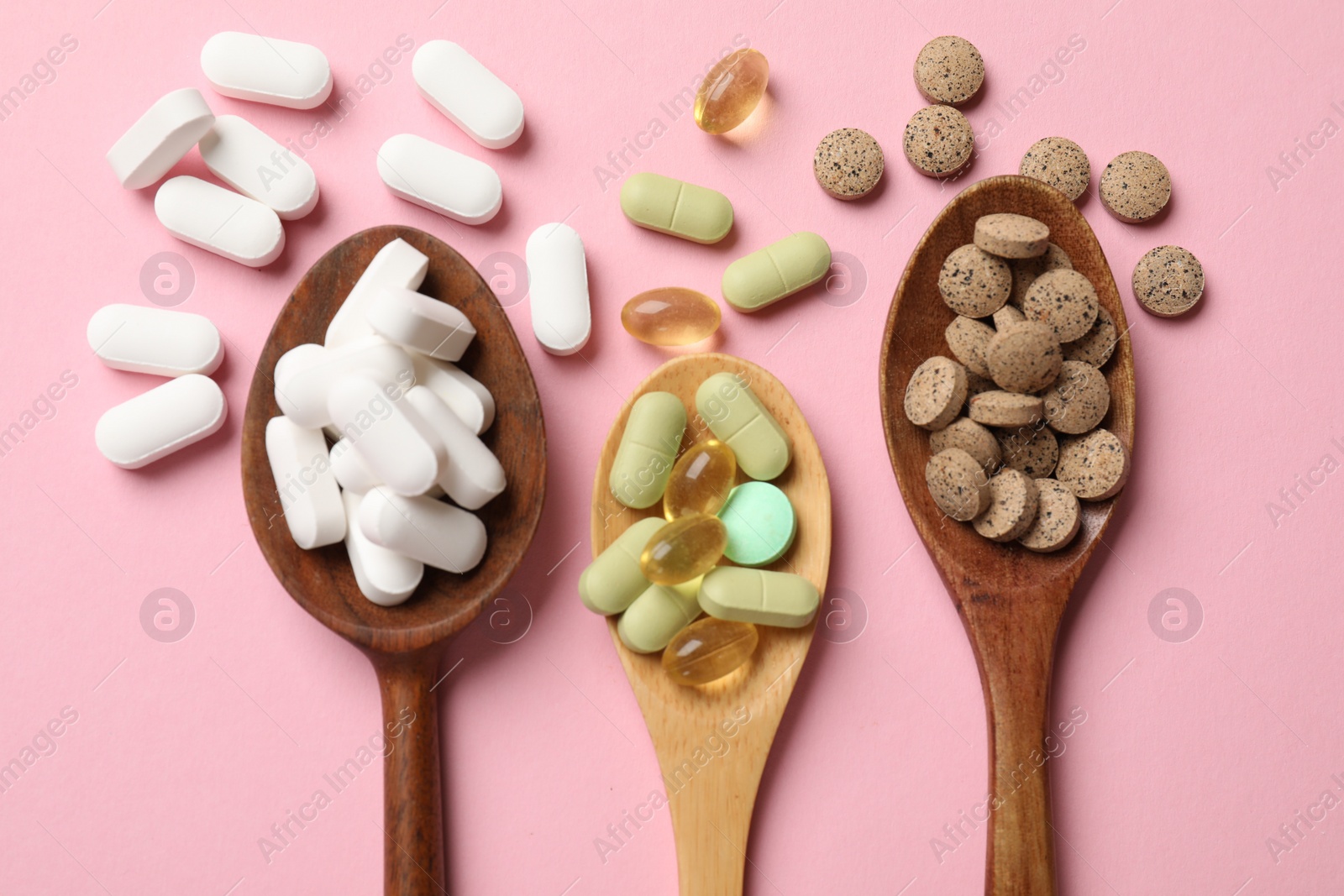 Photo of Different vitamin pills in wooden spoons on pink background, flat lay