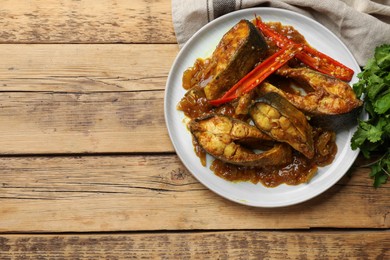 Tasty Indian fish curry on wooden table, top view. Space for text