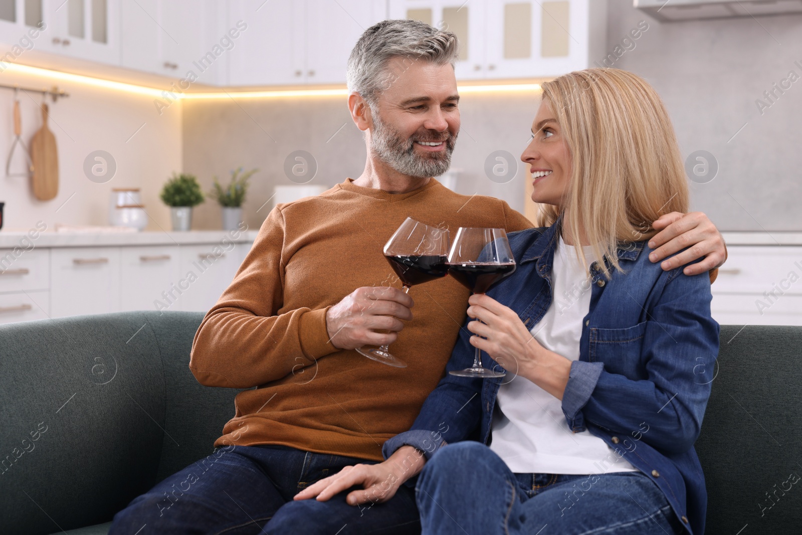 Photo of Happy affectionate couple with glasses of wine on sofa at home. Romantic date