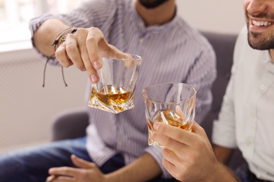 Friends toasting with glasses of whiskey indoors, closeup