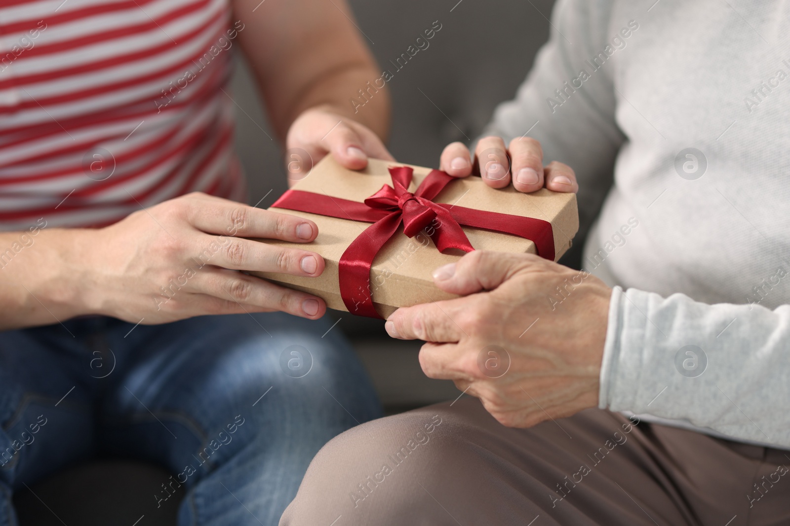 Photo of Son giving gift box to his dad on sofa, closeup