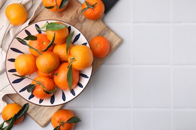 Photo of Fresh ripe tangerines with green leaves on white tiled table, top view. Space for text