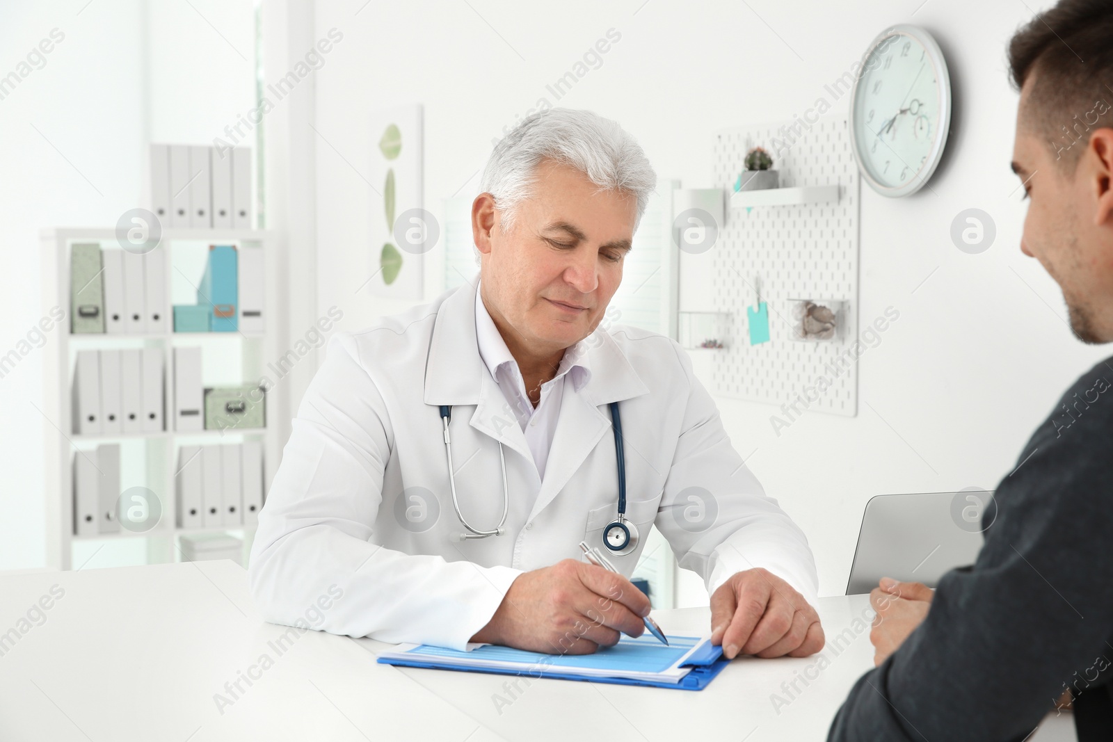 Photo of Senior male doctor working with client at reception desk in hospital