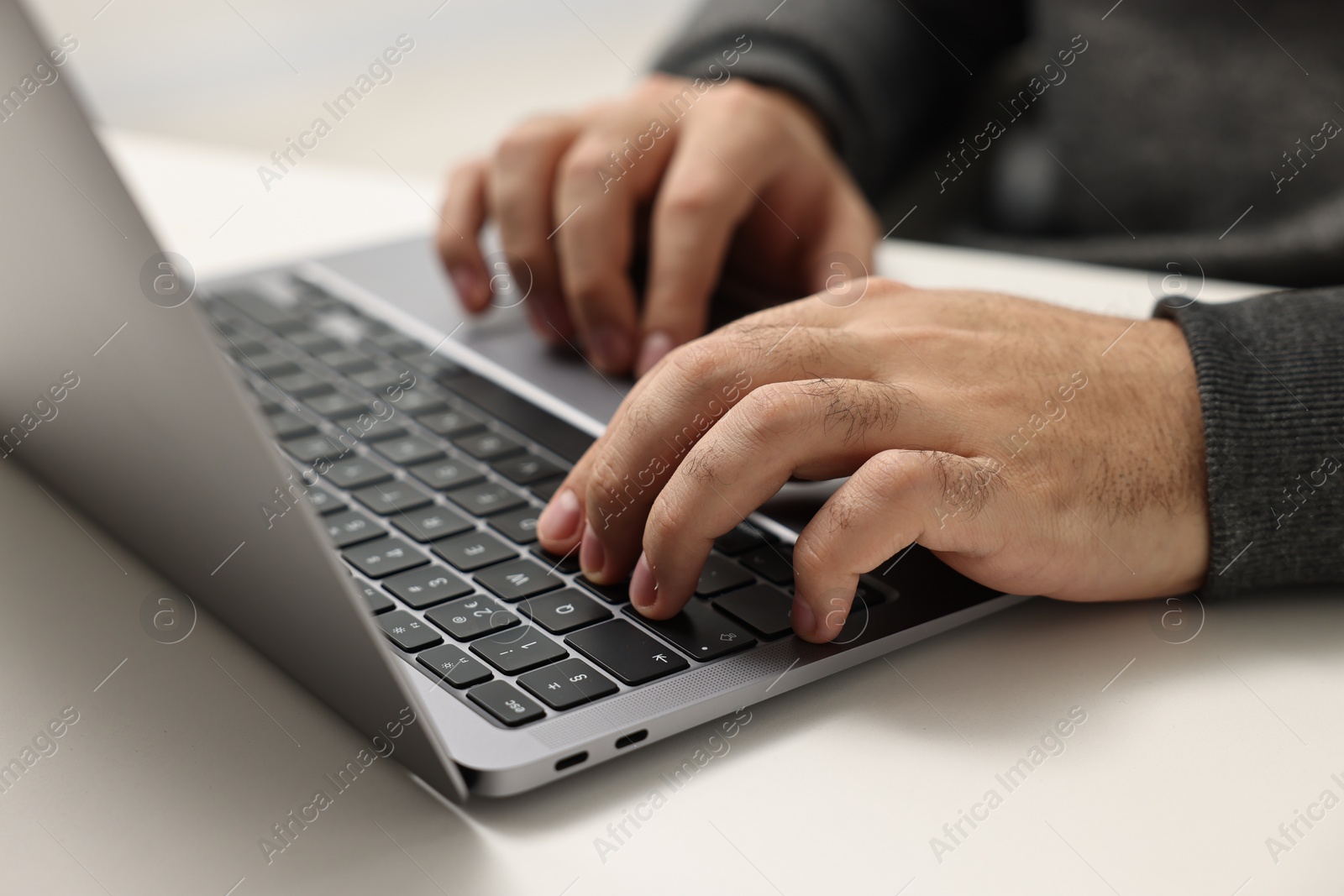 Photo of E-learning. Young man using laptop at white table, closeup