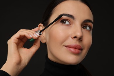 Photo of Beautiful young woman applying mascara on black background, closeup