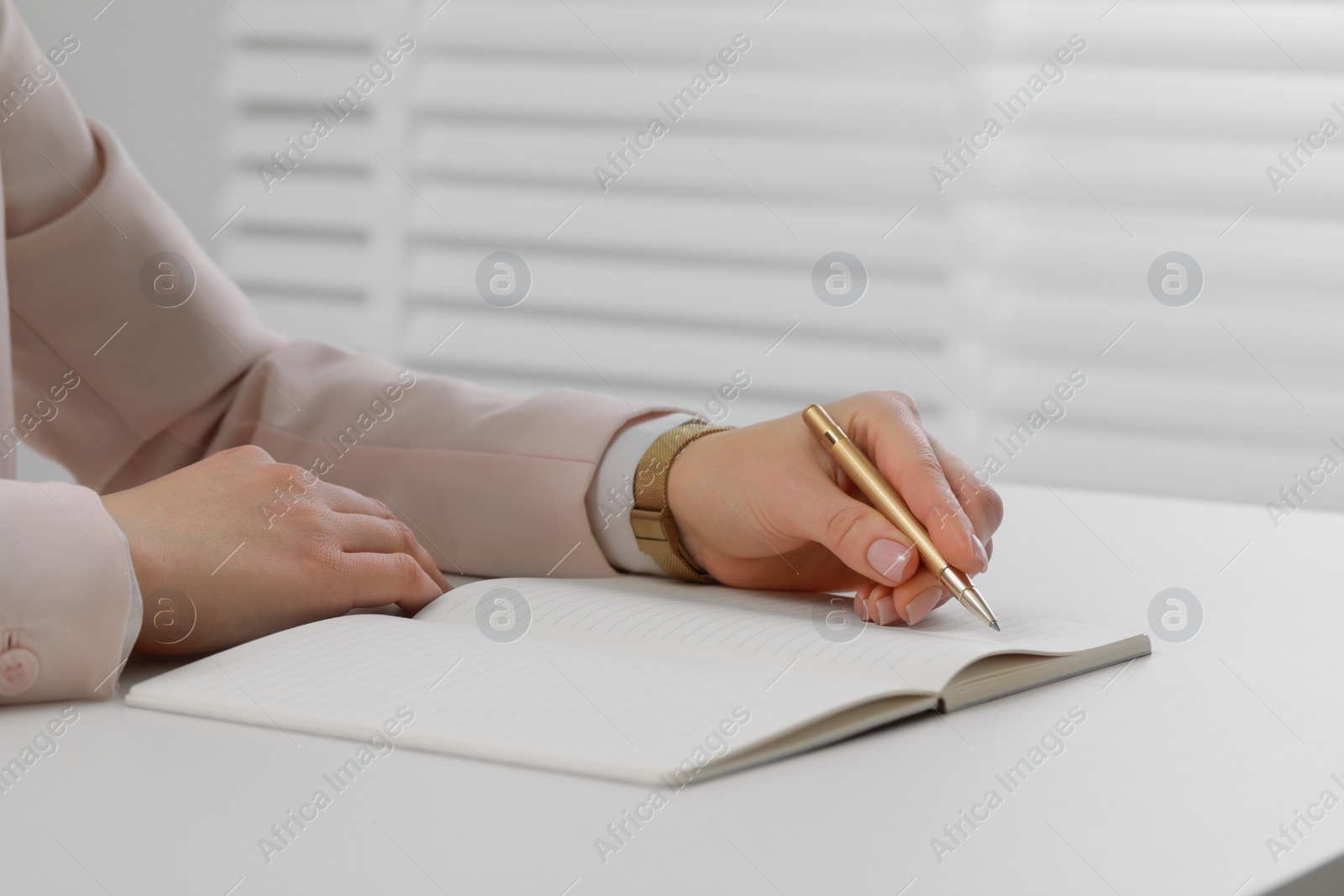 Photo of Woman writing in notebook at white table, closeup