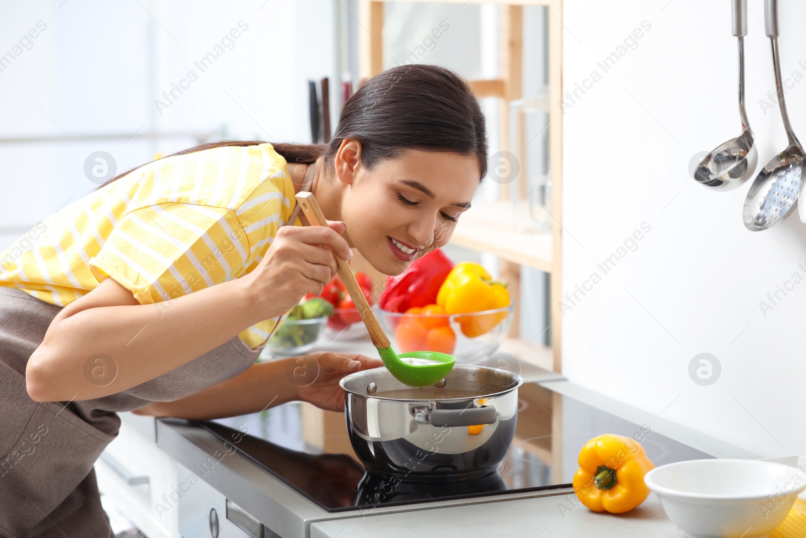 Photo of Young woman cooking tasty soup in kitchen