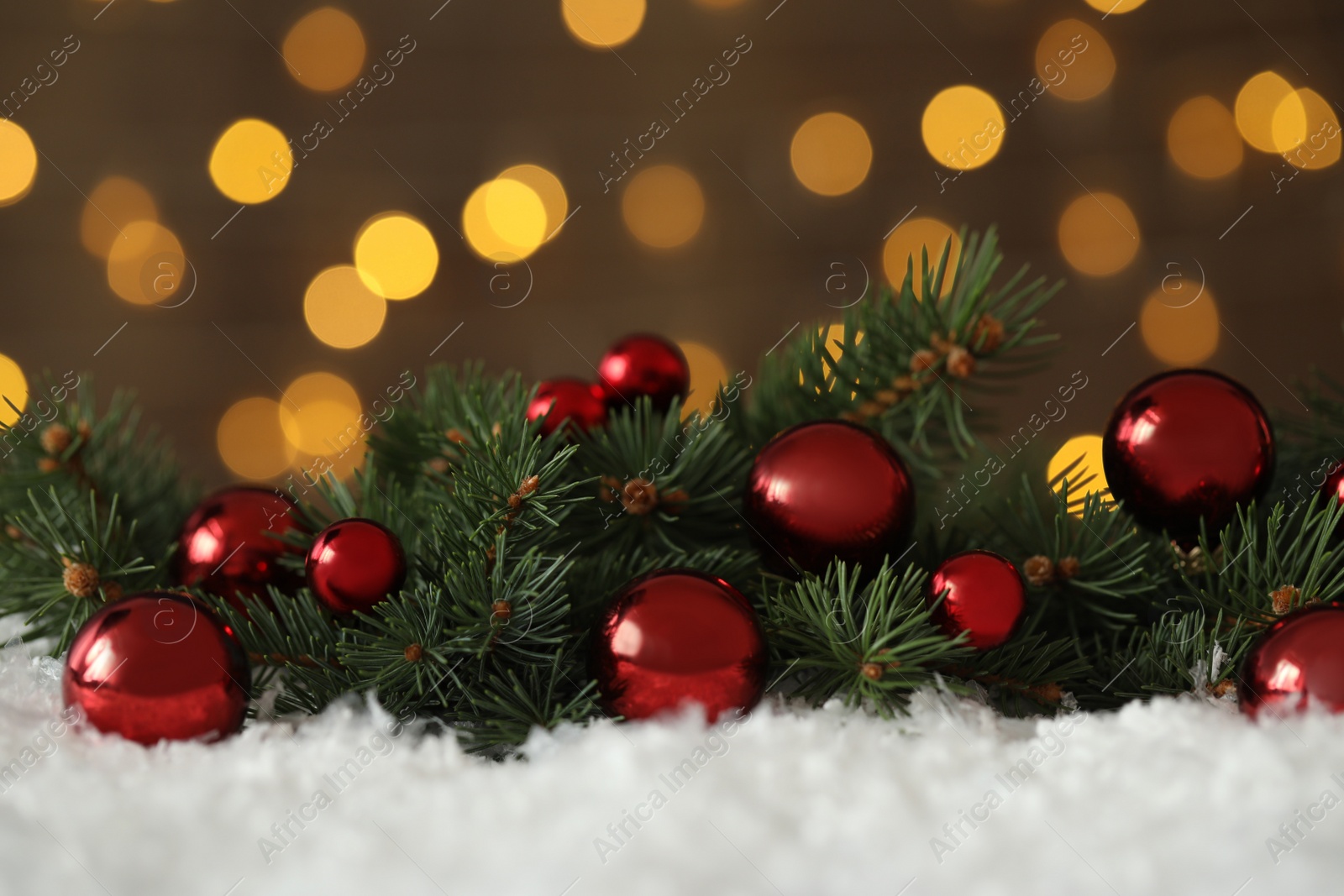 Photo of Fir branches with Christmas balls on snow against blurred festive lights