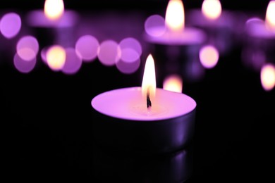 Burning violet candle on black background, closeup. Funeral attributes