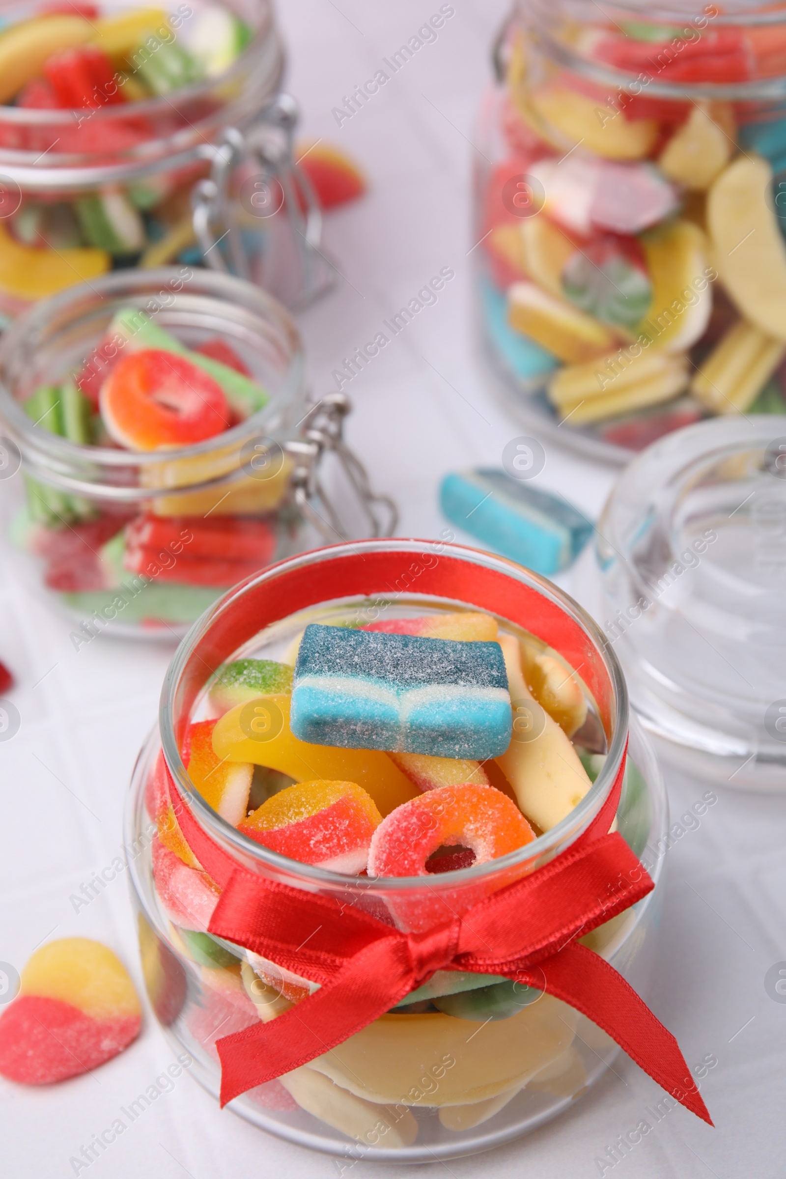 Photo of Glass jars with tasty colorful jelly candies on white tiled table, closeup