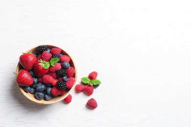 Photo of Bowl with raspberries and different berries on wooden table, top view