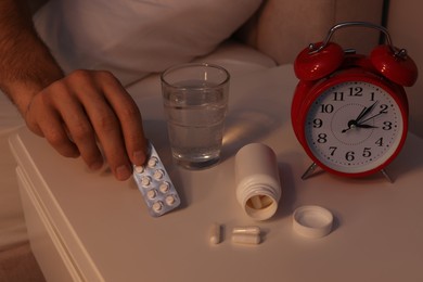 Man suffering from insomnia taking pills in bed at night, closeup