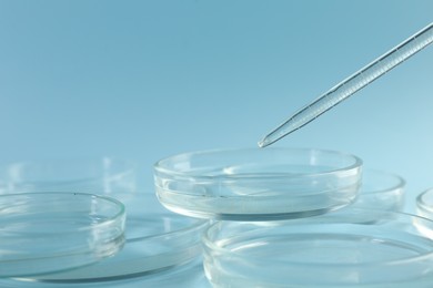Photo of Pipette over petri dish on light blue background, closeup
