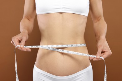 Photo of Slim woman measuring waist with tape on brown background, closeup. Weight loss