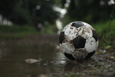 Dirty leather soccer ball in puddle outdoors, space for text