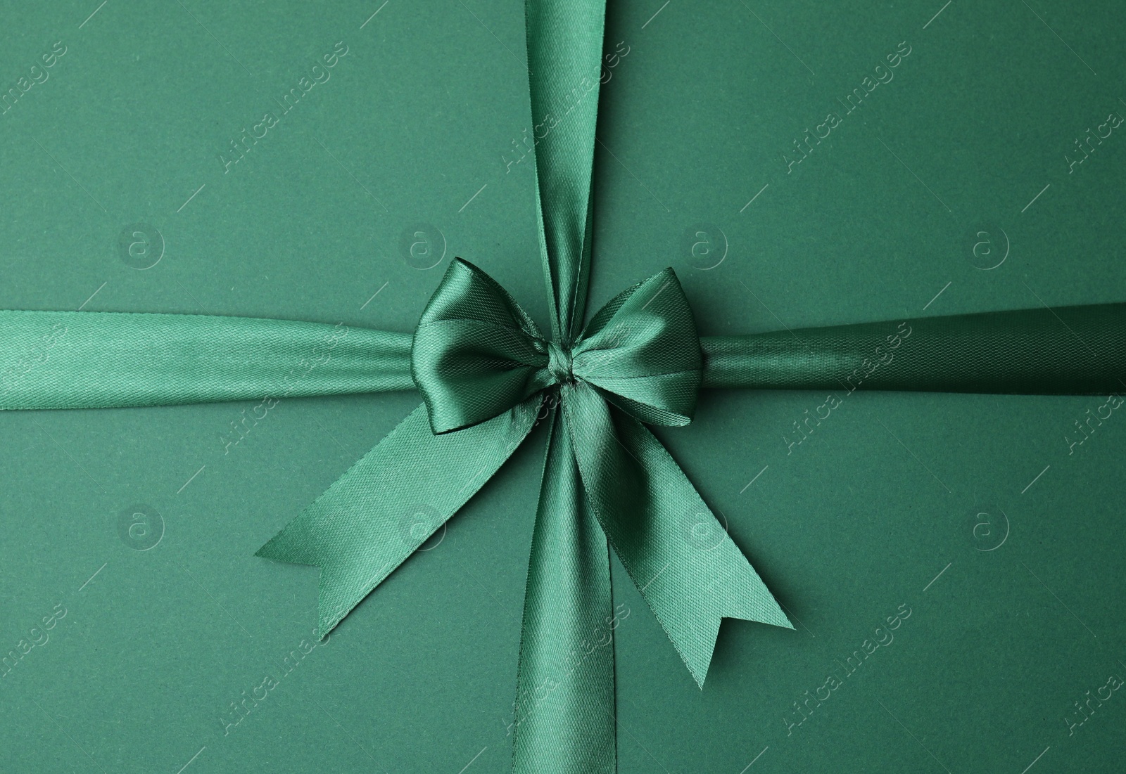 Photo of Bright satin ribbon with bow on green background, top view