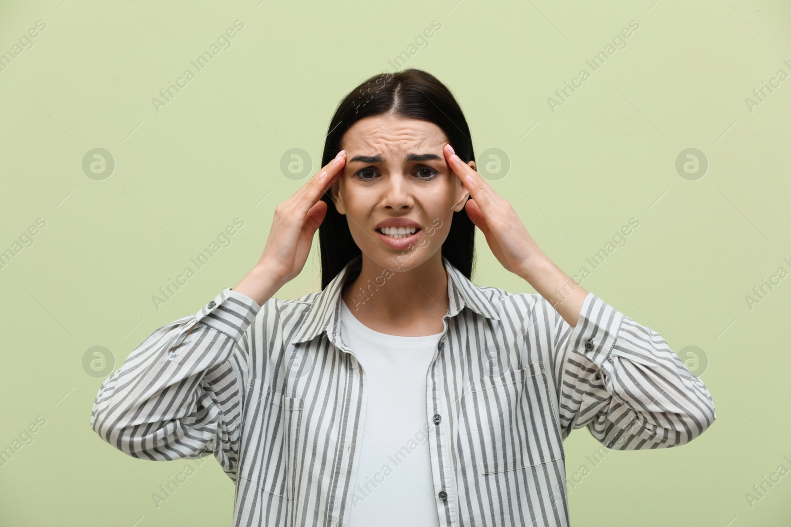 Photo of Woman suffering from migraine on light green background