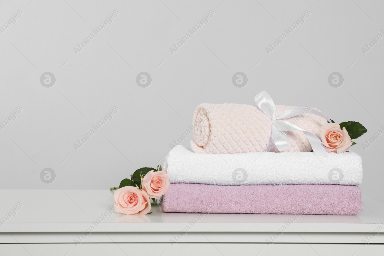 Photo of Clean soft towels with flowers on white table against light grey background. Space for text