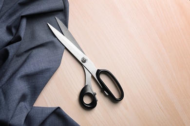 Photo of Scissors and fabric for tailoring on light wooden background