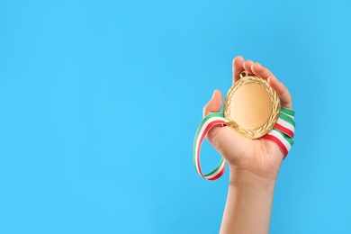 Photo of Woman holding gold medal on light blue background, closeup. Space for text