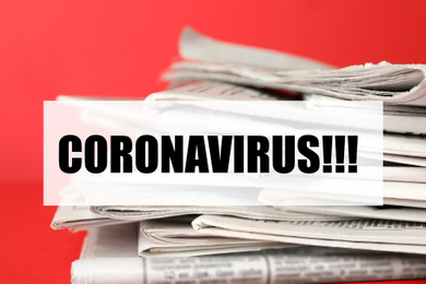 Image of Word CORONAVIRUS and stack of newspapers on red background, closeup. Journalist's work