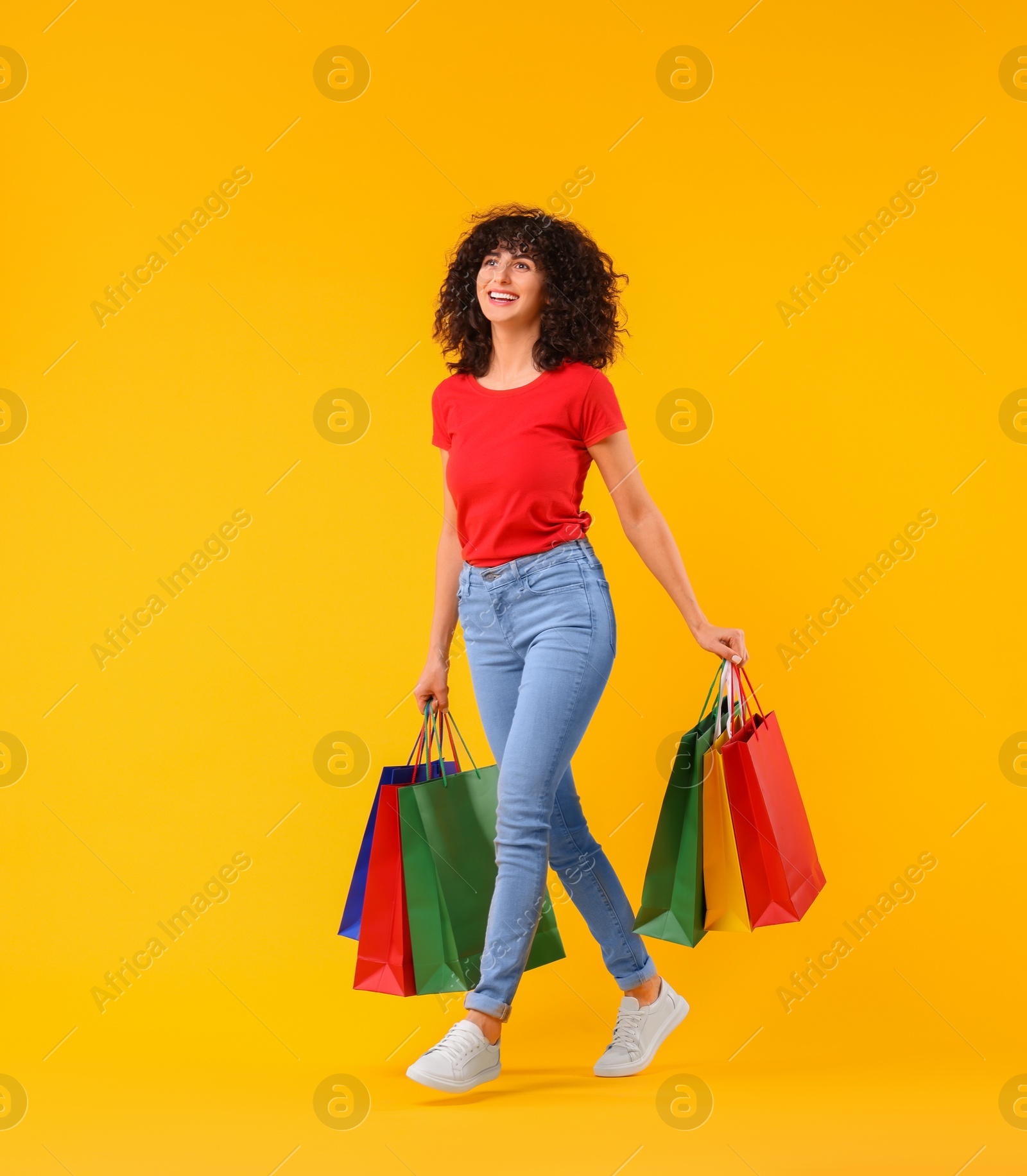 Photo of Happy young woman with shopping bags on yellow background. Space for text