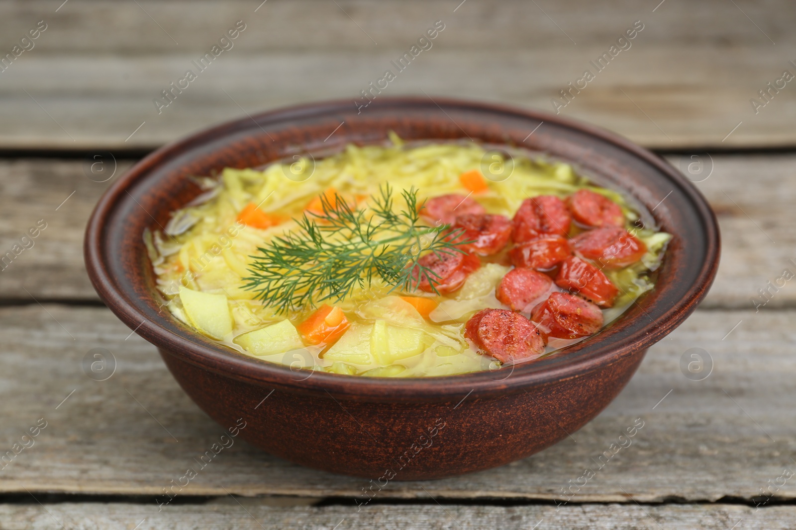 Photo of Bowl of delicious sauerkraut soup with smoked sausages and dill on wooden table