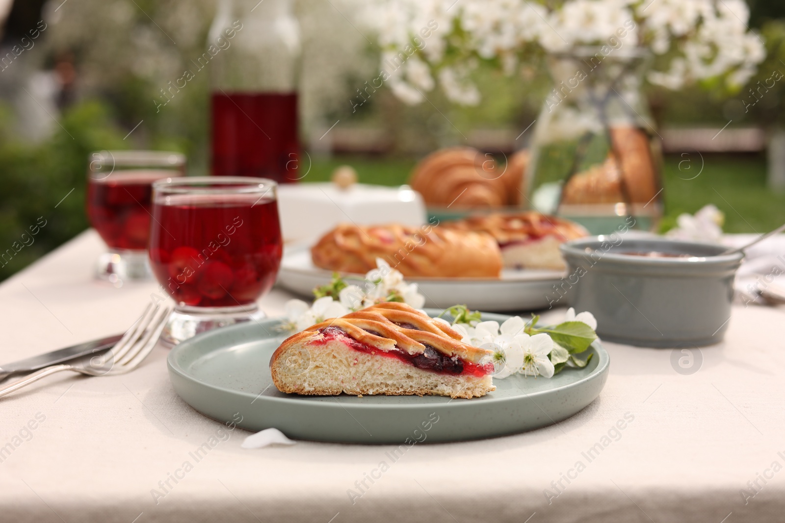 Photo of Stylish table setting with beautiful spring flowers, fruit drink and pie in garden