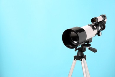 Tripod with modern telescope on light blue background, closeup. Space for text