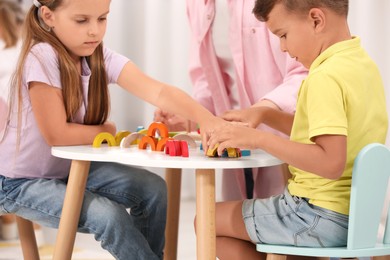 Photo of Little children and nursery teacher playing with colorful wooden pieces at desk in kindergarten. Playtime activities for motor skills development