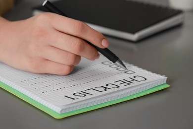 Photo of Woman filling Checklist with pen at grey table, closeup