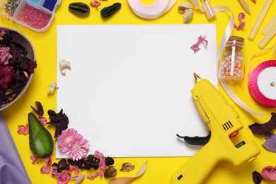 Hot glue gun and handicraft materials on yellow background, flat lay. Space for text